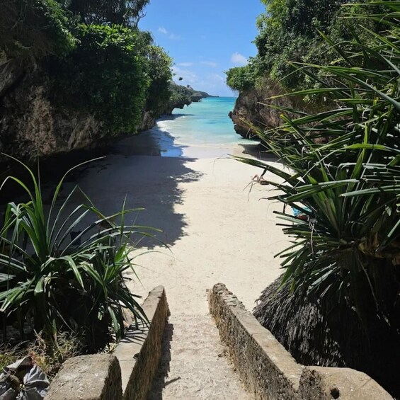 A coastal pathway leading to a beach with clear turquoise waters, surrounded by lush greenery and rocky cliffs. 1