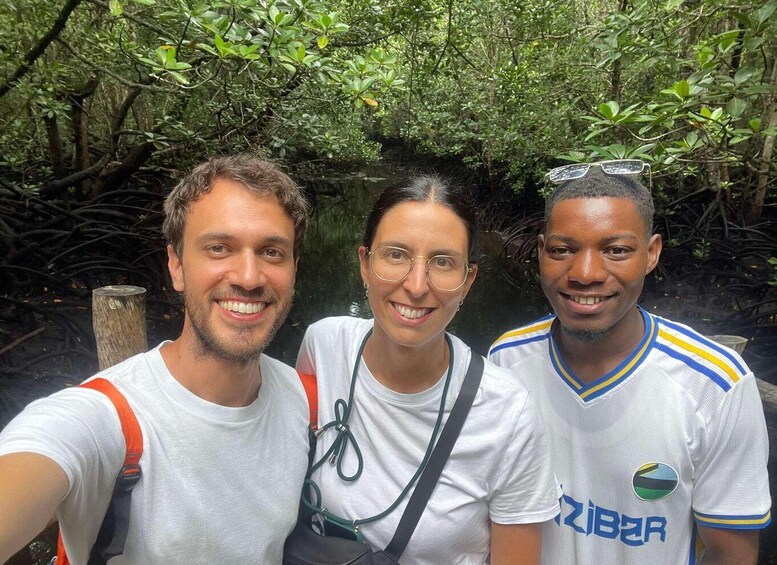 Three people in a natural setting with dense foliage and a wooden structure. 2
