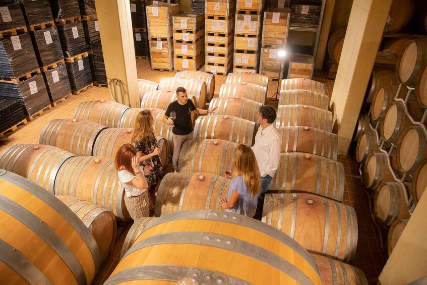 A group of people in a wine cellar surrounded by large wooden barrels. 2