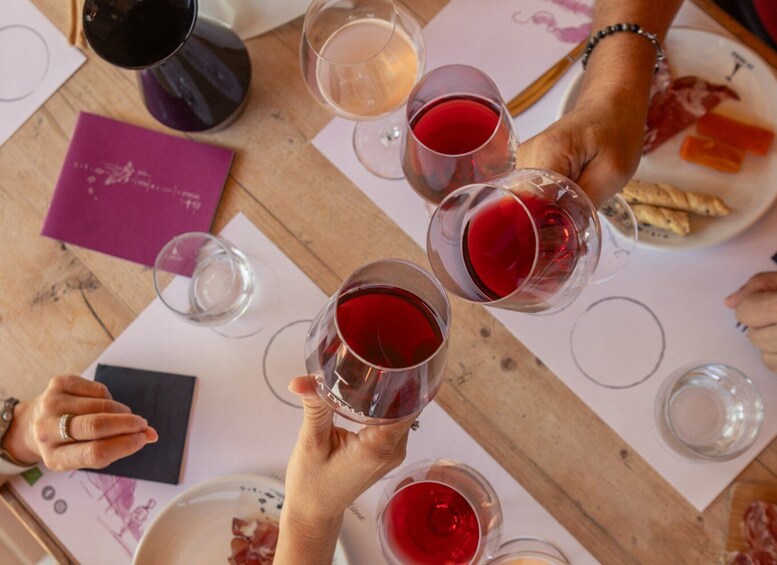 A group of people toasting with red wine glasses at a wooden table with a purple menu and plates of food. 4