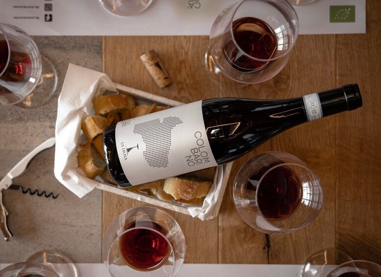 A bottle of wine with a label, surrounded by glasses and bread on a wooden table. 3