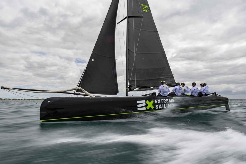 Una barca a vela nera con la scritta 'EXTREME SAILING' sul fianco, che corre sull'acqua. 4