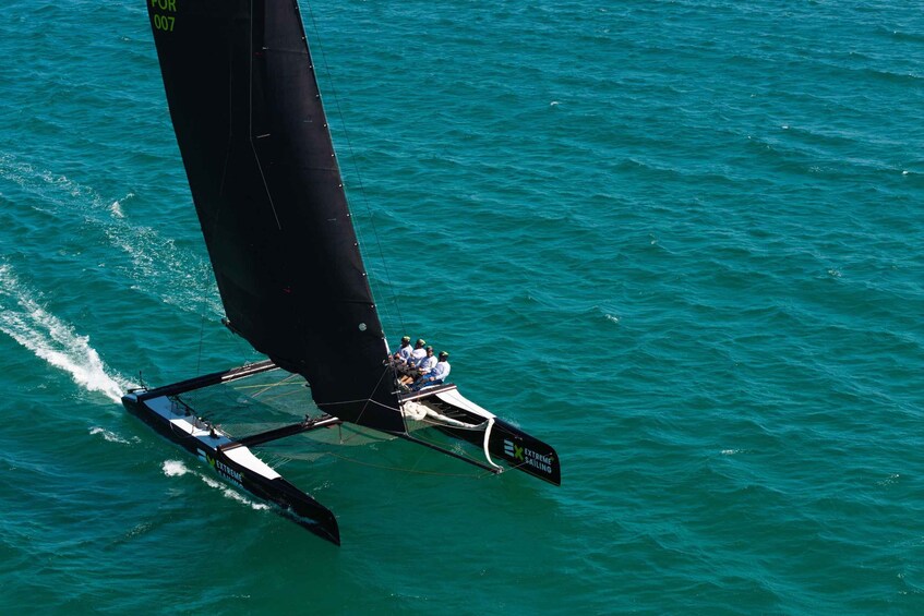 Una barca a vela con una vela nera e la scritta 'EXTREME SAILING' sul fianco, che naviga in acque turchesi. 5