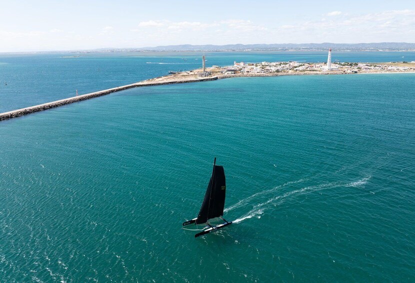 Una barca a vela su acque turchesi, con un faro e una costa rocciosa sullo sfondo. 1