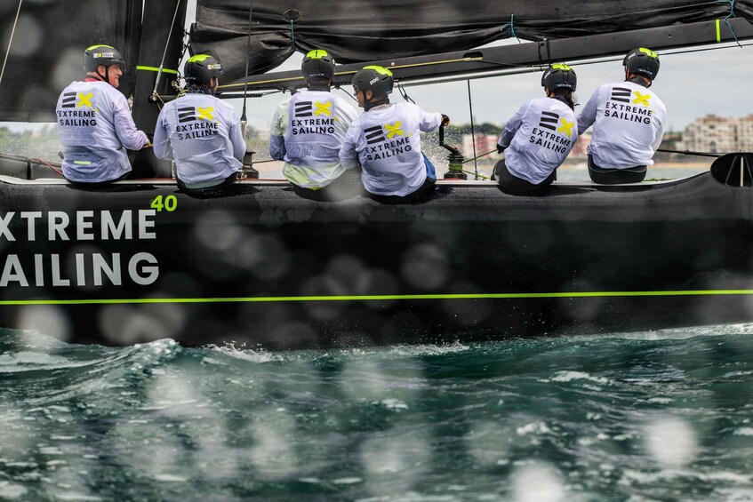 Un gruppo a bordo di un'imbarcazione a vela con la scritta 'EXTREME SAILING' sulle magliette, che indossano caschi e il numero '40' sullo scafo. 2