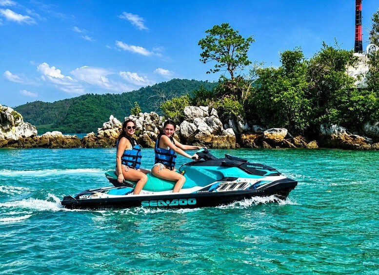 Two people on a jet ski in turquoise water with a rocky shoreline and greenery in the background. 5