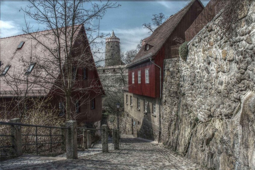 A cobblestone street flanked by historic buildings with stone walls and a tower. 3