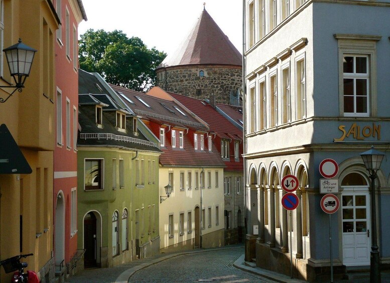 A narrow cobblestone street lined with colorful buildings, a church with a red roof, and a sign for 'SALON' on the right. 2