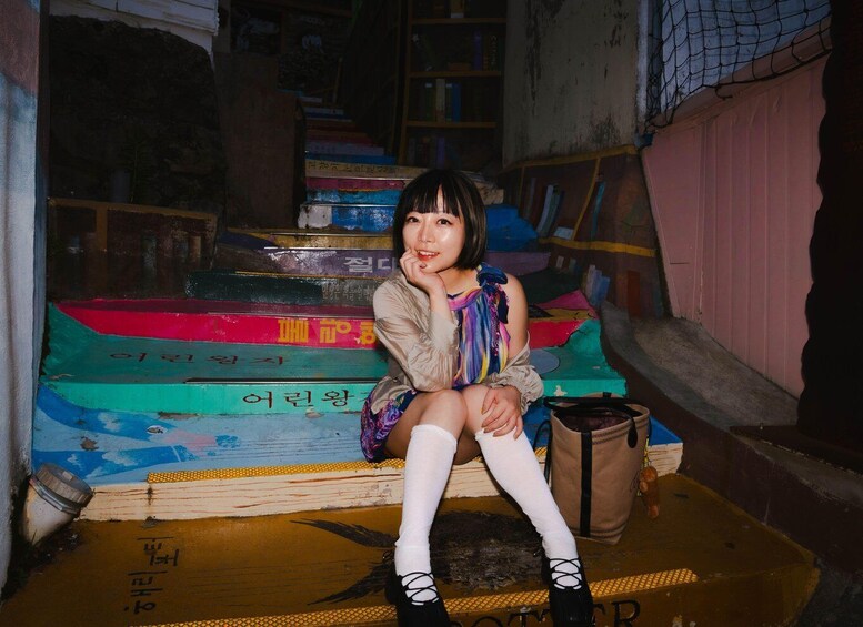 A person sitting on a colorful staircase with books and a bag. 4