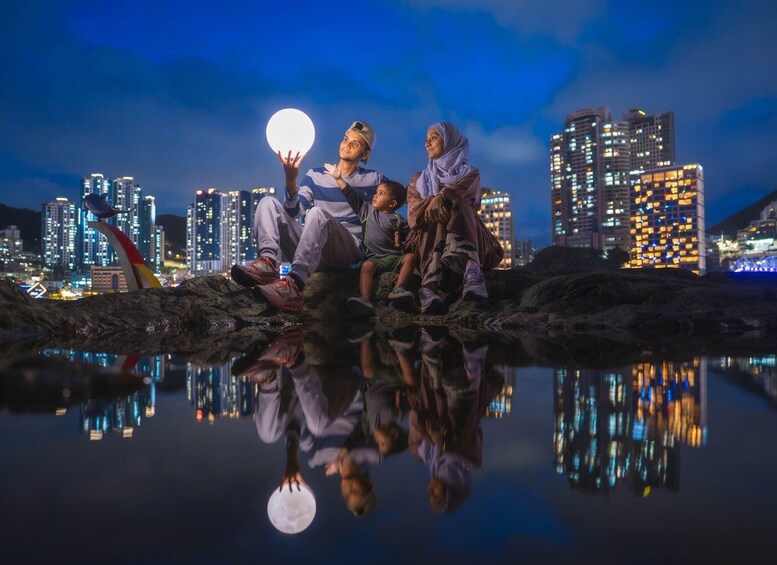 A group of people sitting on rocks with a cityscape and a full moon in the background. 1