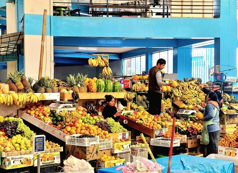 A bustling indoor market with various fruits and vegetables on display, including bananas, pineapples, and melons. 2