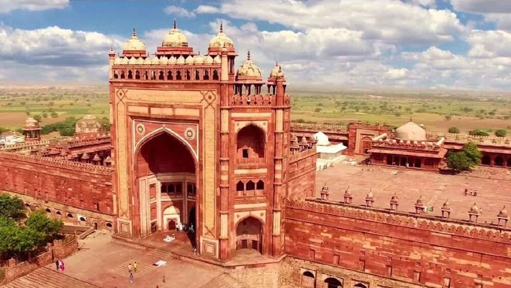 A large red sandstone gateway with domes, surrounded by a vast open landscape. 4