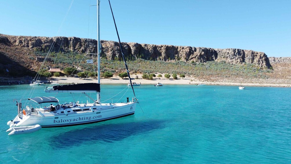 A sailboat named 'Sun Odyssey 49' anchored near a rocky coastline with clear turquoise water. 1