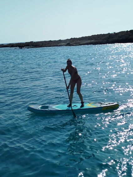 A person paddleboarding on a calm sea with a rocky shoreline in the background. 5