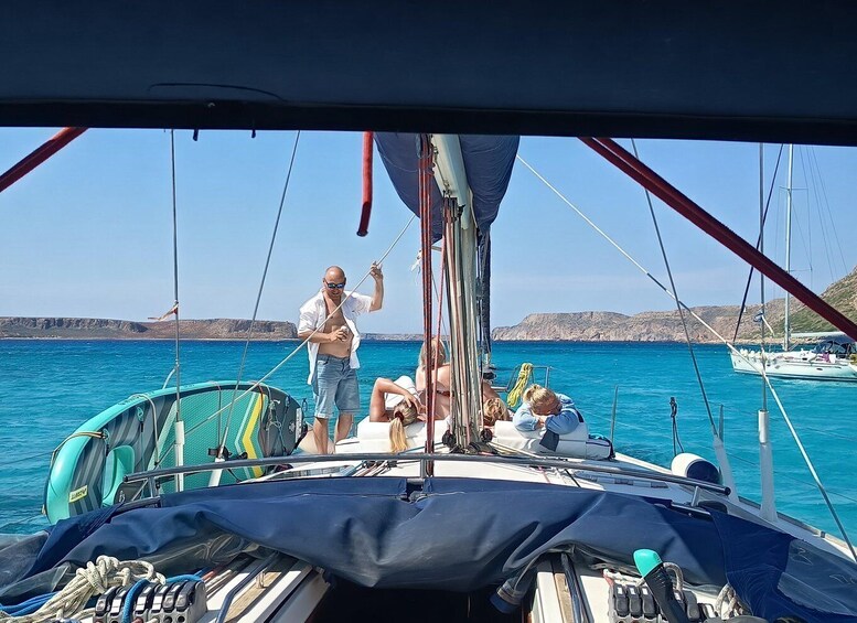 A sailboat with people on deck, calm sea, and rocky coastline in the background. 2