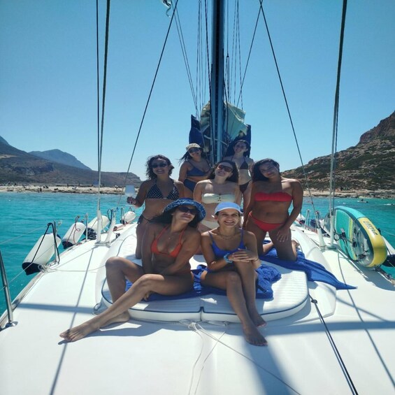 A group of people on a sailboat with a clear blue sea and rocky hills in the background. 4