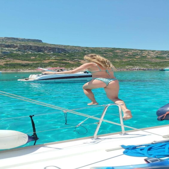 A person in a bikini standing on a boat's deck, with a clear blue sea and a rocky coastline in the background. 5