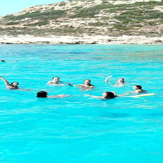 A group of people swimming in a turquoise sea with a rocky coastline in the background. 3