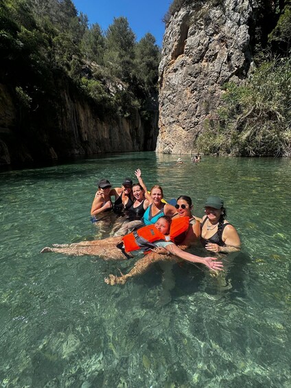 A group of people in a clear river surrounded by rocky cliffs and greenery. 4