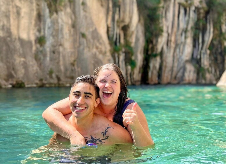 Two people embracing in a clear blue pool with rocky cliffs in the background. 1