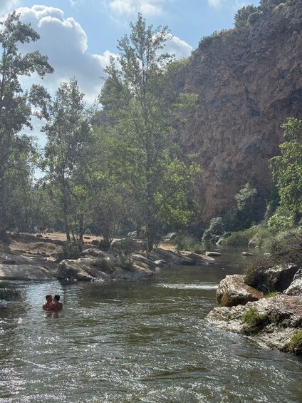 A river with rocks and trees, a person in a kayak, and a rocky cliff. 5