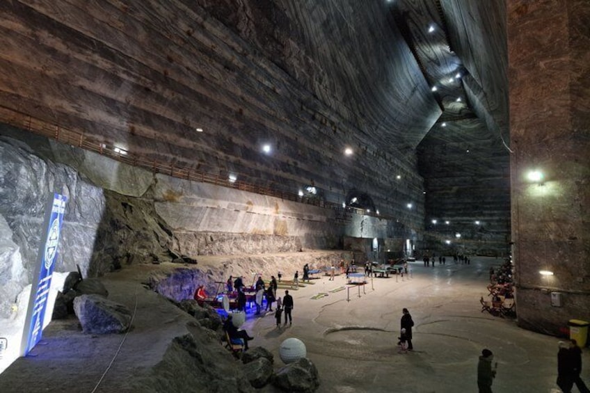 An indoor cave with rock formations, a large open space, and people exploring. 1