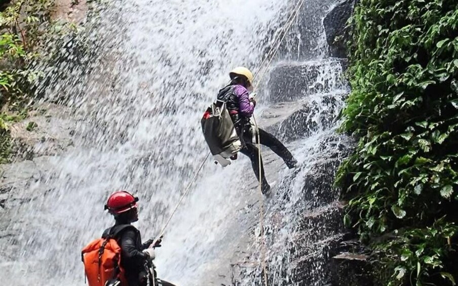 A person rappelling down a waterfall with a backpack. 1