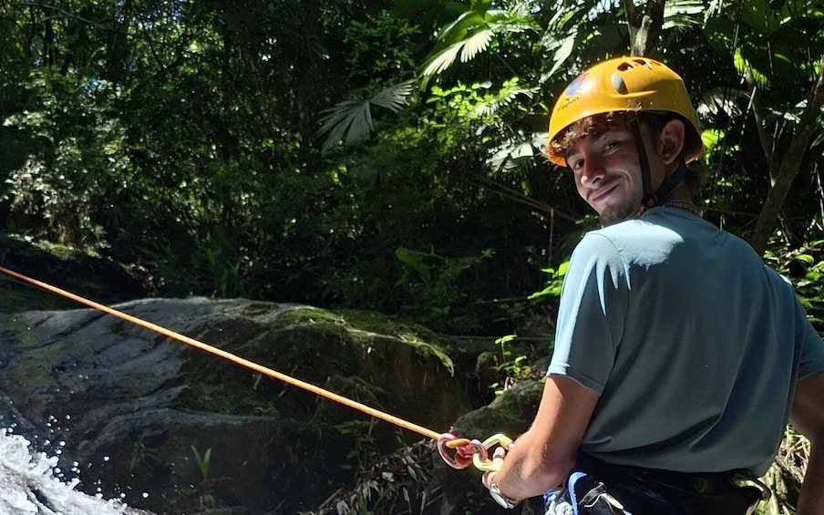 A person rappelling down a rocky water body surrounded by dense foliage. 4