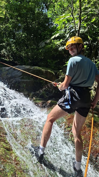 A person rappelling down a waterfall in a forested area. 3