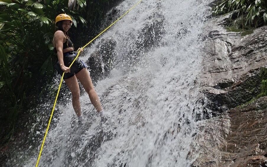 A person rappelling down a waterfall surrounded by dense foliage. 2
