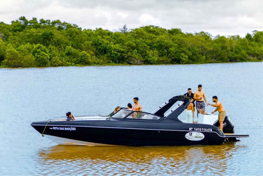 A black speedboat with people on board, surrounded by calm water and dense green foliage in the background. 1