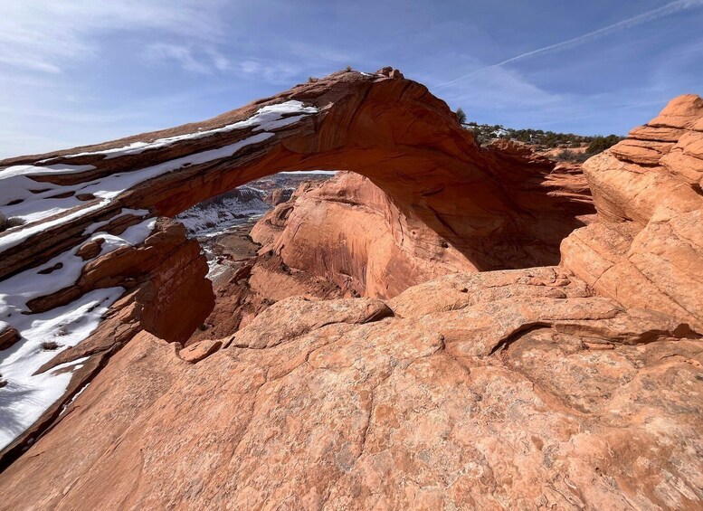 A large red rock arch with snow patches on the ground. 2