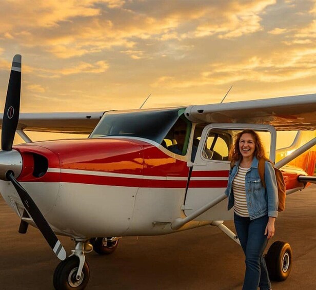 A small red and white propeller plane on the tarmac with a person standing beside it. 1