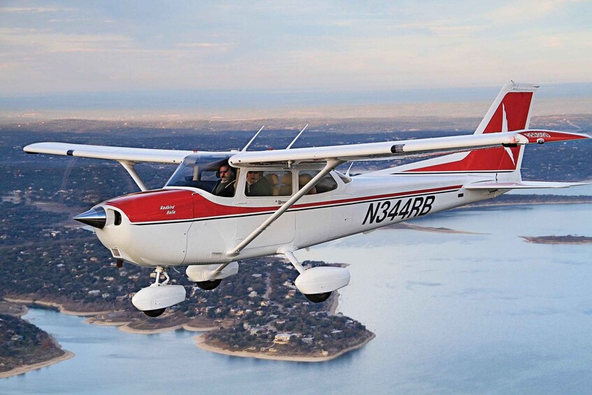 A red and white single-engine aircraft with the registration N344BB flying over a coastal area with visible land and water. 2