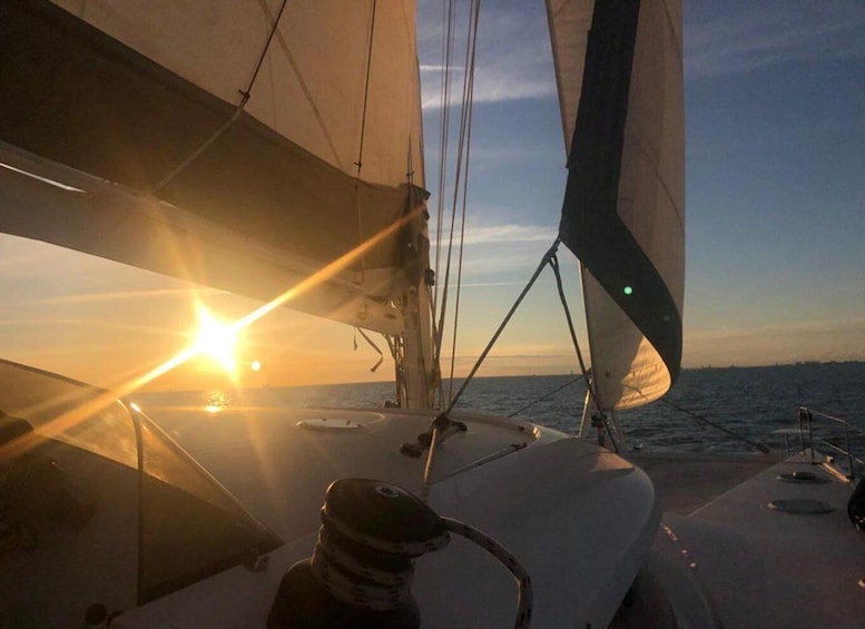 A sailboat with sails unfurled, heading towards a sunset over the ocean. 1