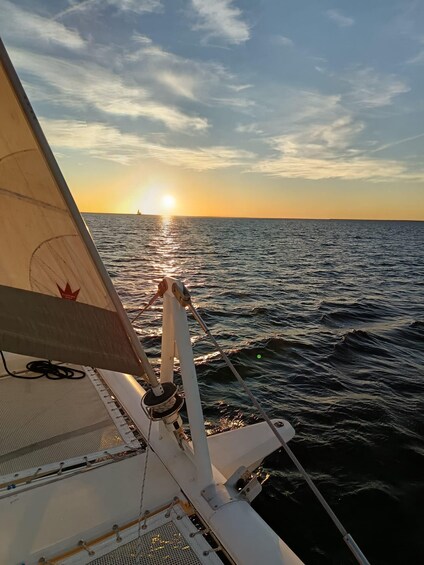 A sailboat's sail and rigging with the sun setting over the ocean. 4
