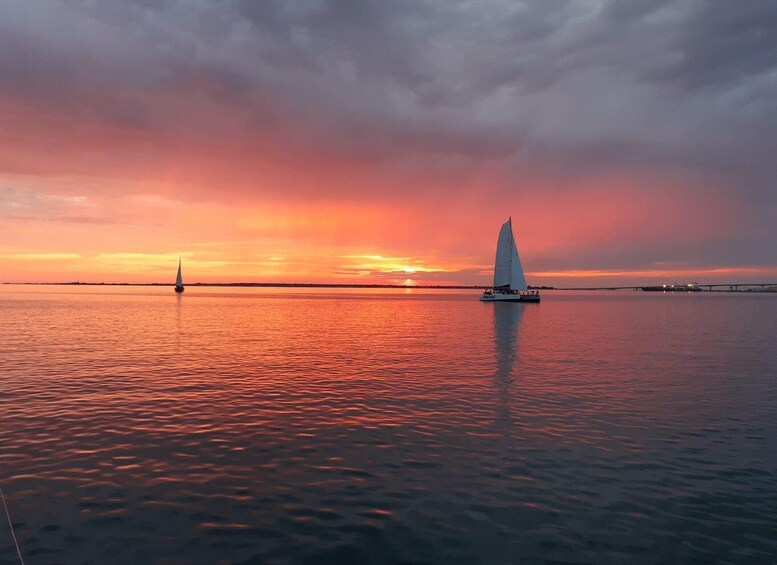 A sailboat on calm waters during sunset with a bridge in the background. 3