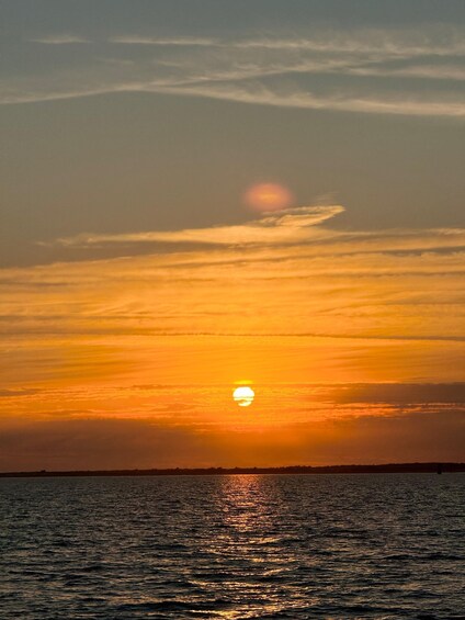 A sunset over a body of water with the sun partially obscured by clouds. 1