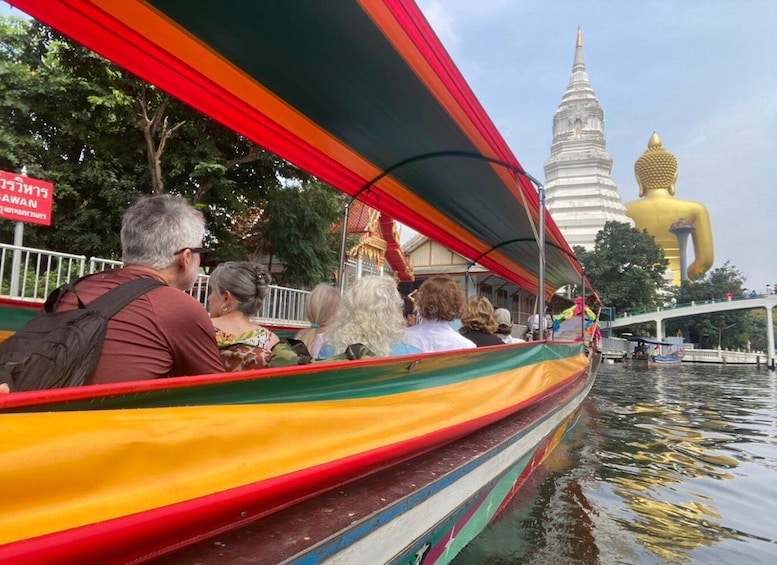 A group of people on a colorful boat, a white temple with a golden statue, and a bridge in the background. 1