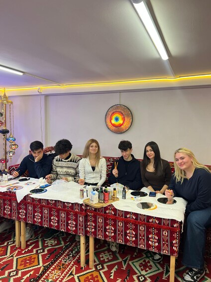 A group of people engaged in a creative activity at a table with art supplies and a patterned tablecloth. 2