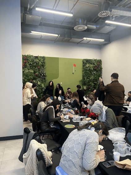 A group of people seated around a table in a room with green walls and ceiling lights. 3