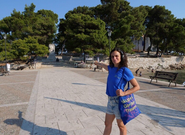 A person standing in a park with a sign reading 'Skiathos Garden Theatre.' 2