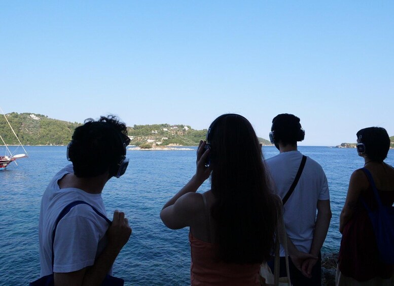 A group of people standing by a body of water, looking at a sailboat and a distant shoreline with buildings. 5