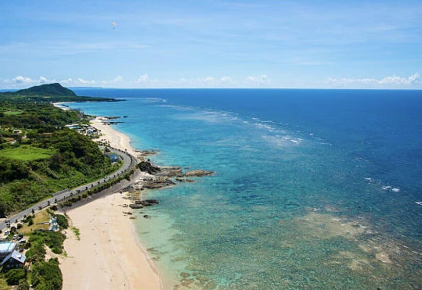 A coastal landscape with a beach, clear waters, and a road curving along the shore. 5