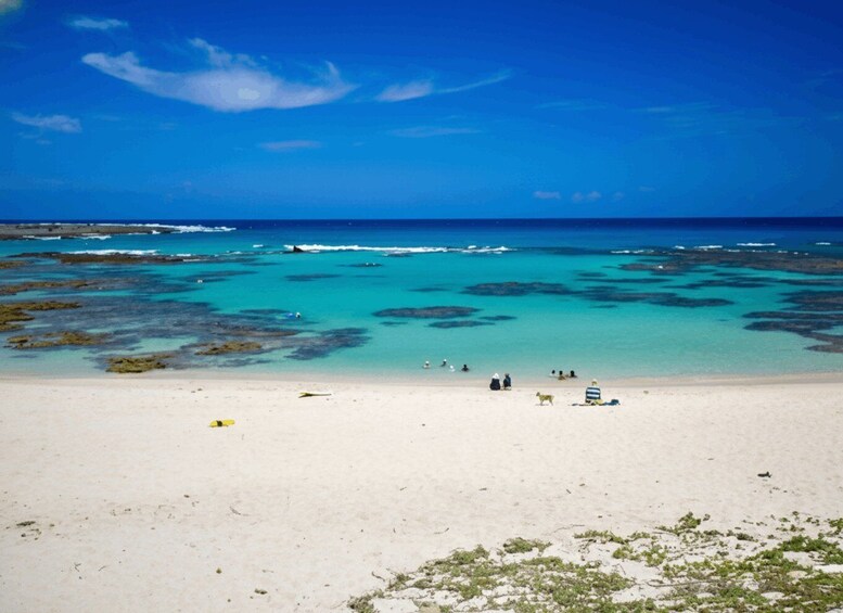 A beach with clear turquoise water, white sand, and scattered rocks. 3