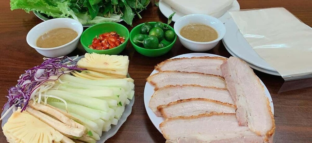 Sliced pork, fresh herbs, and dipping sauces on a wooden table. 1