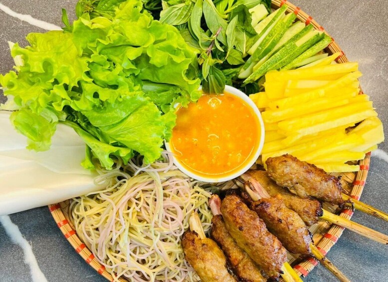 A plate with noodles, lettuce, grilled meat skewers, and a bowl of sauce. 3