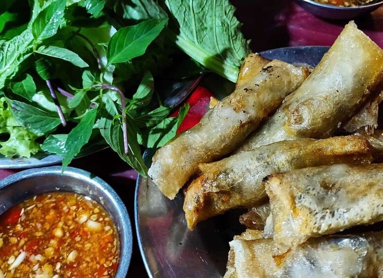 A plate of fried spring rolls with a side of dipping sauce and fresh herbs. 5
