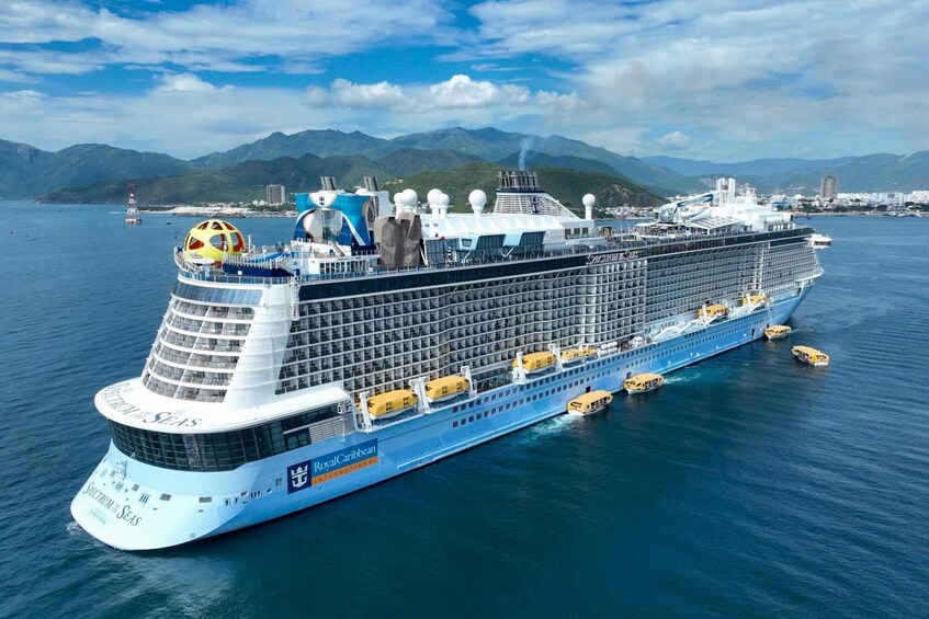 A large cruise ship named 'Royal Caribbean' sailing in the ocean with mountains in the background. 5