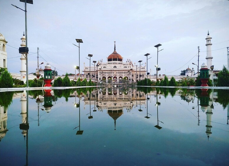 A grand building with a large dome, surrounded by a reflective water body, with street lamps and a mosque in the background. 1